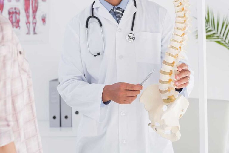 Person holding their lower back beside a staircase while another person observes their posture