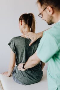 A clinician explains a spine model while a seated patient reviews treatment options in a bright examination room.