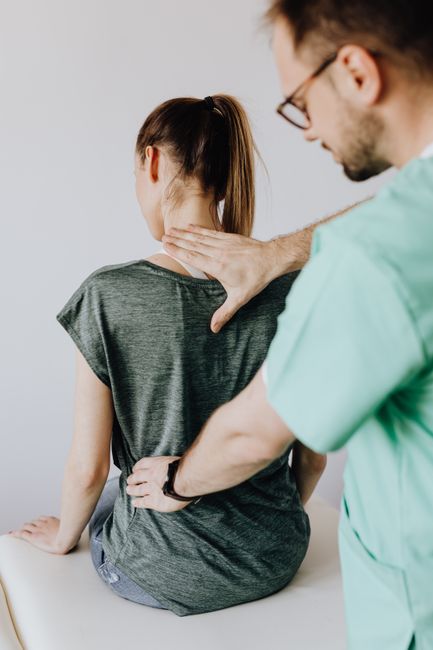 A clinician explains a spine model while a seated patient reviews treatment options in a bright examination room.